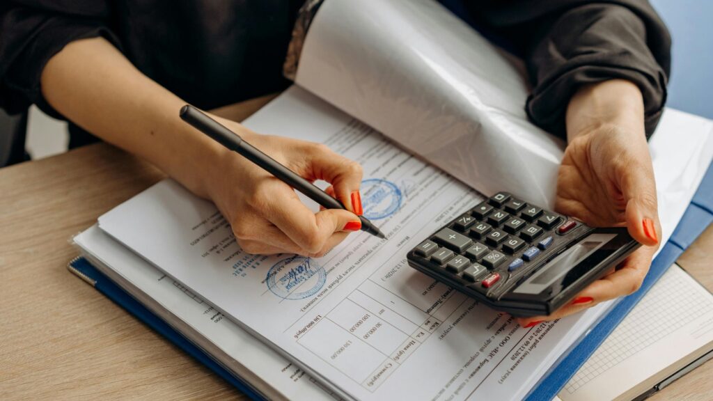 A woman using a calculator working through a detailed payroll compliance checklist on her desk